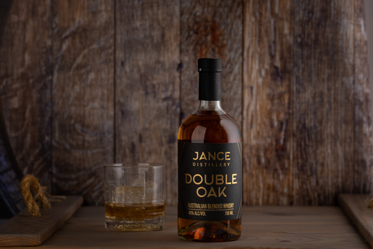 A photo of the Jance Double Oak whisky and an old fashioned glass against a wood backdrop.